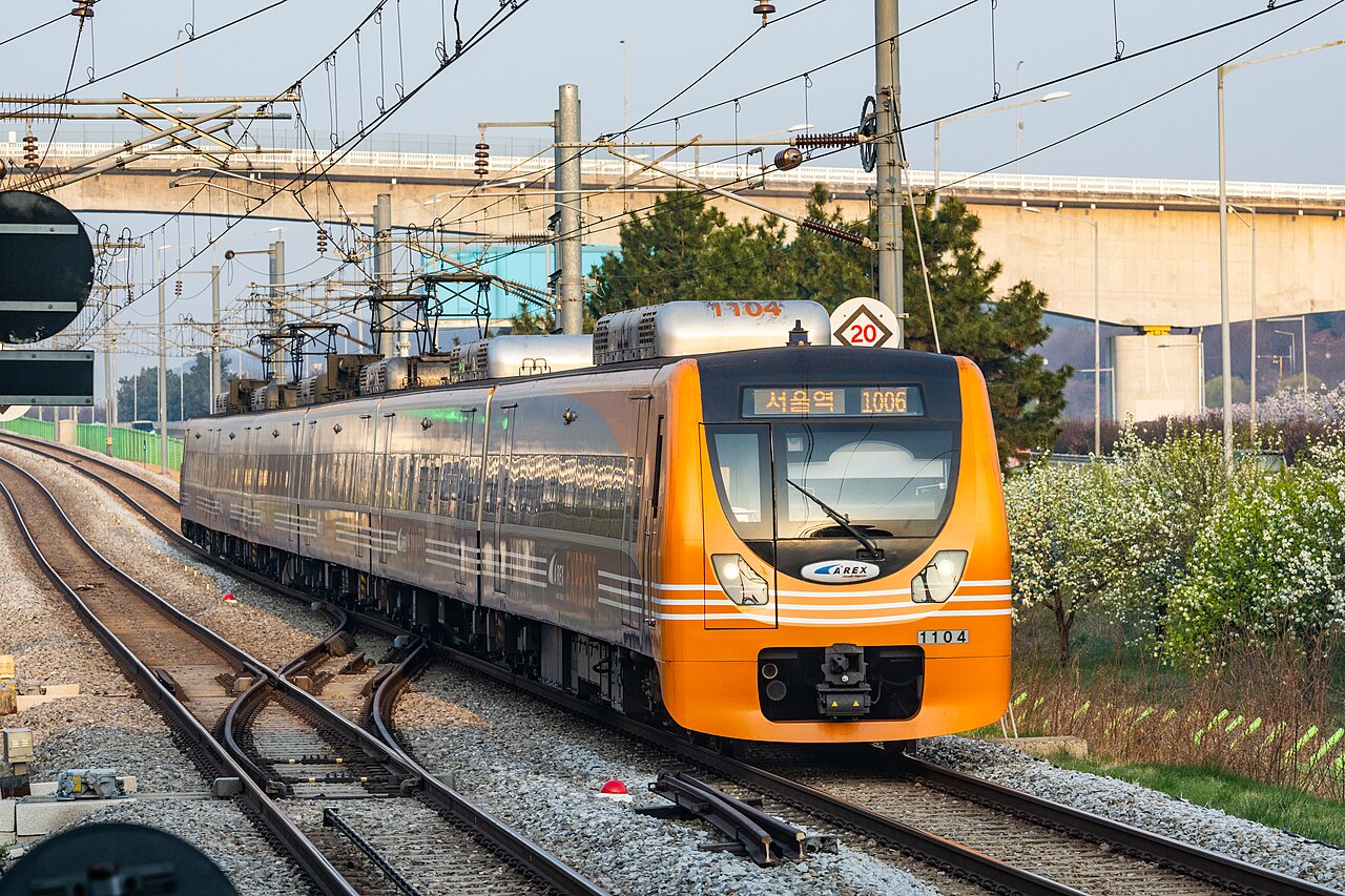 An orange AREX express train bound for Seoul Station approaches Gyeyang on railway tracks.