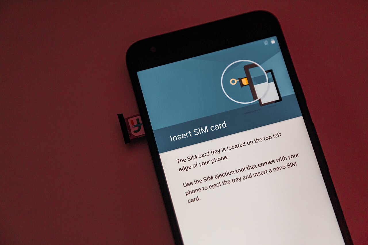 A smartphone on a red surface with its physical SIM tray partly ejected and an Insert SIM card message on screen.
