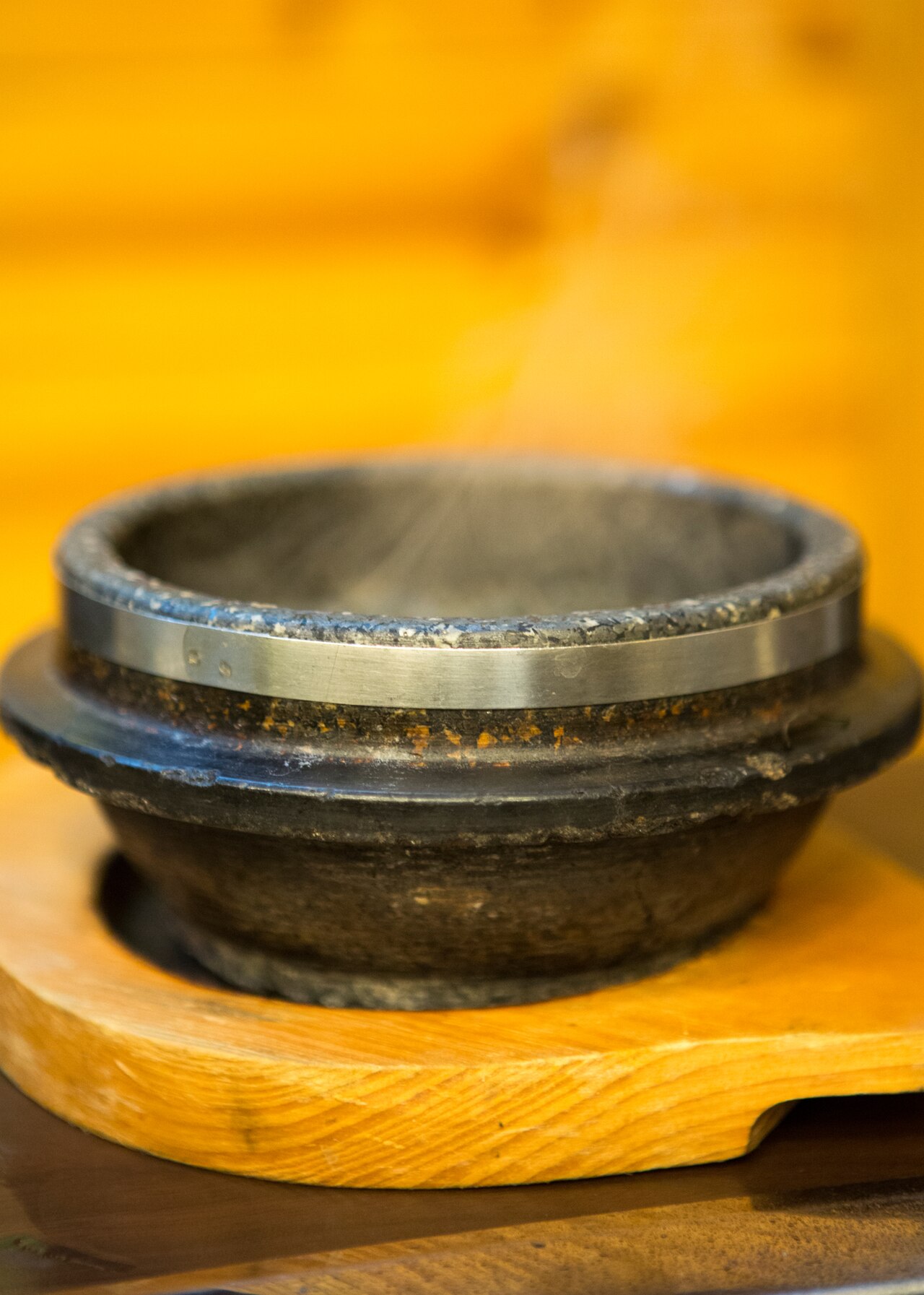 An empty grey stone dolsot pot with a metal band around the rim sitting on a round wooden base.