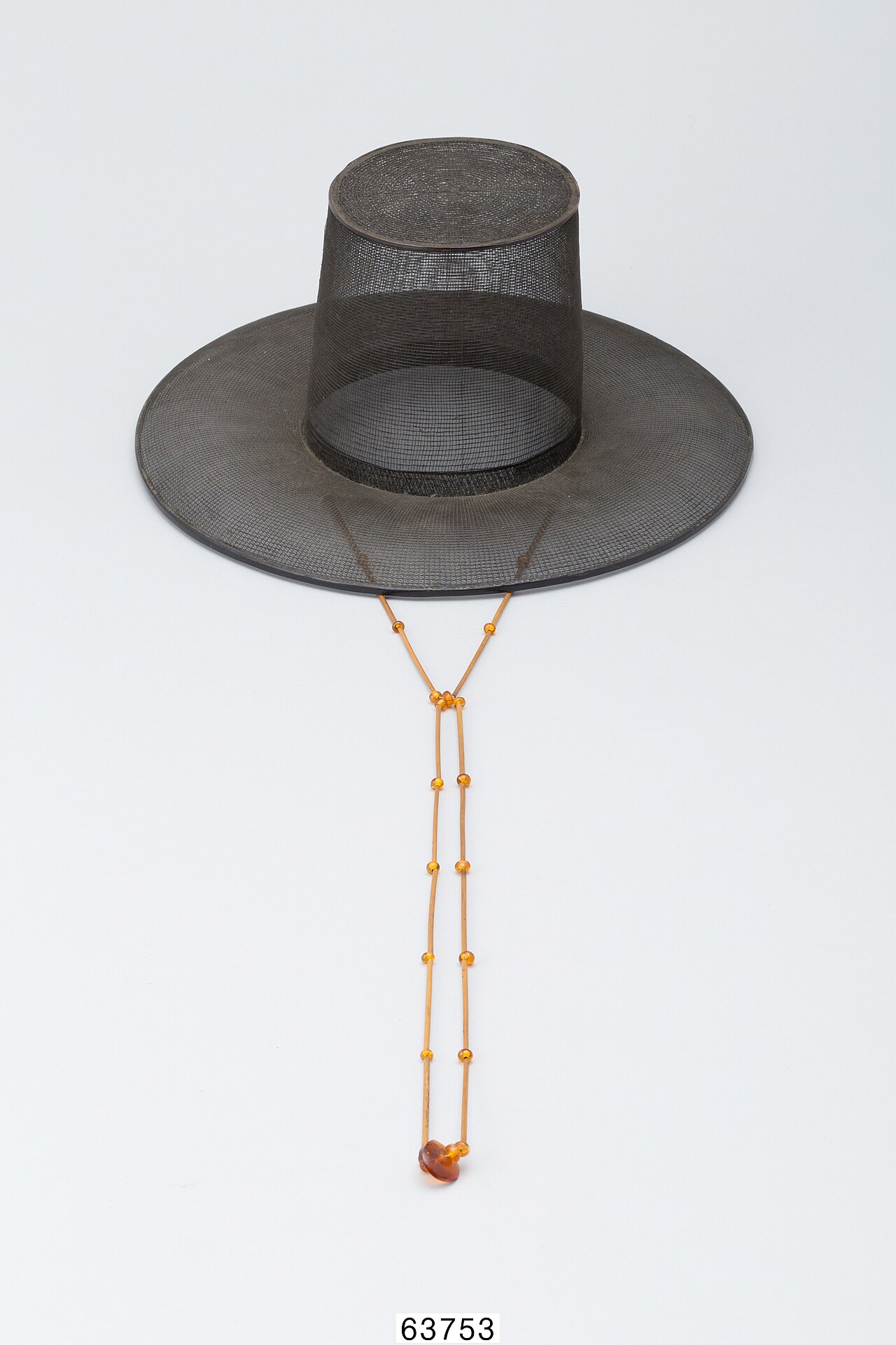 A black horsehair gat with a wide brim and a long amber-coloured beaded chin strap hanging below it.