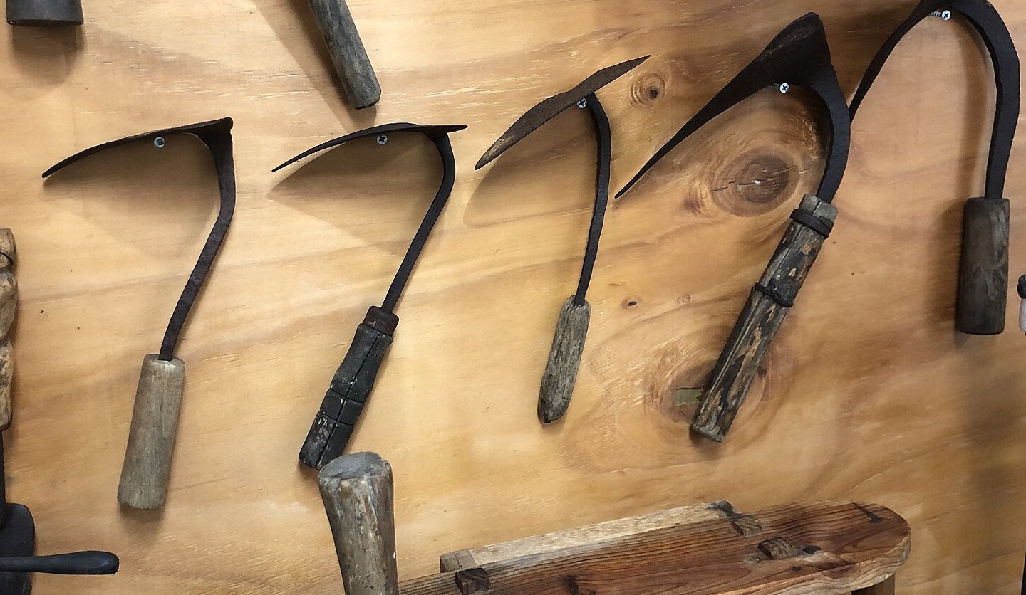 Five old Korean homi hand hoes with different blade shapes mounted on a wooden wall.