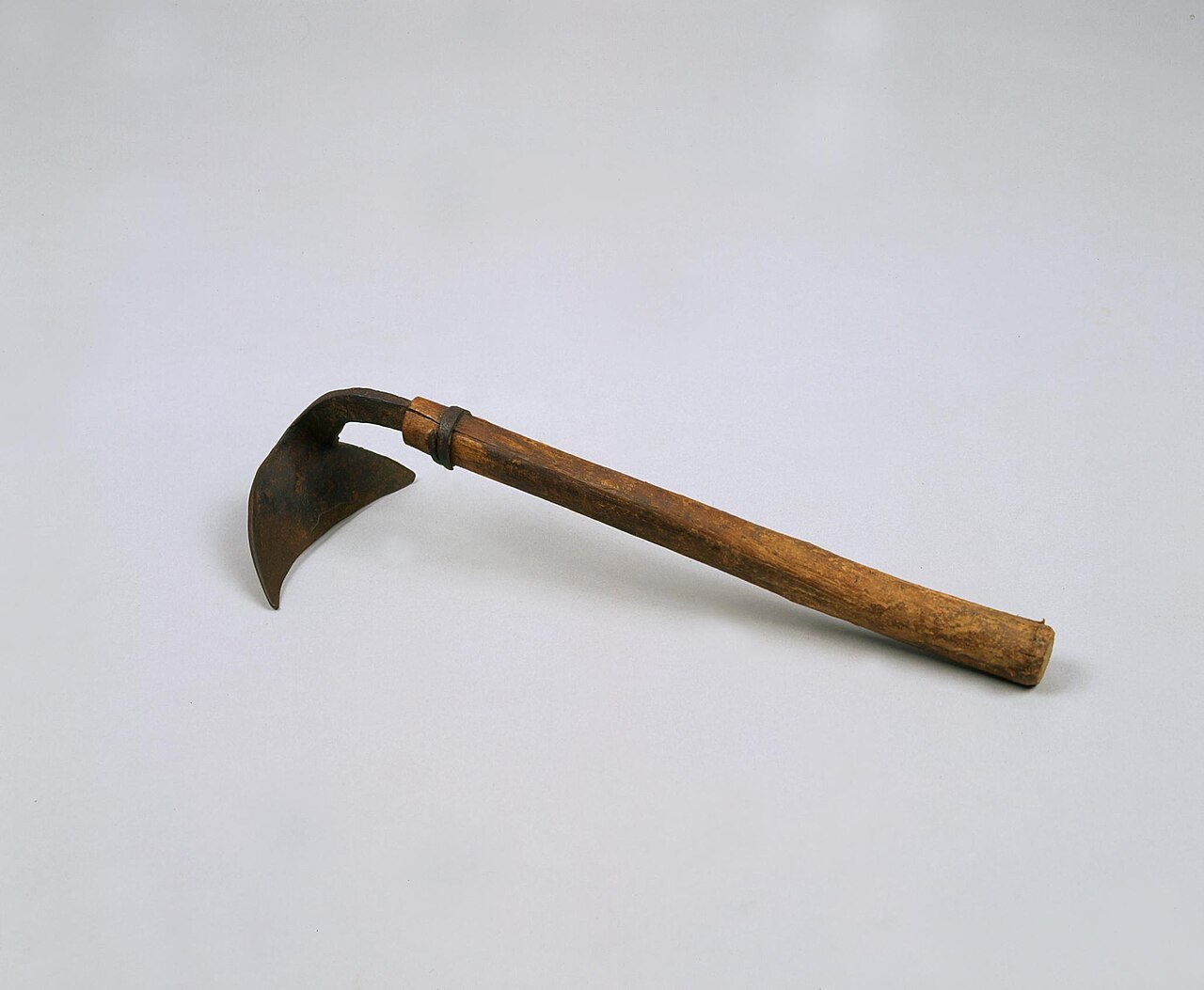 A Korean homi hand hoe with a curved, pointed iron blade and a wooden handle on a plain grey background.
